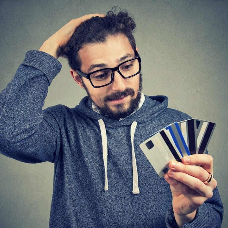 Young male student with glasses holding multiple credit cards looking stressed about his climbing debt